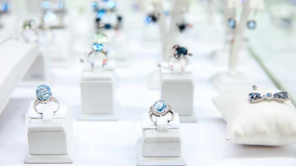 An elegant display of jewelry featuring sparkling rings with blue gemstones, set against a bright white background in a well-lit showcase.