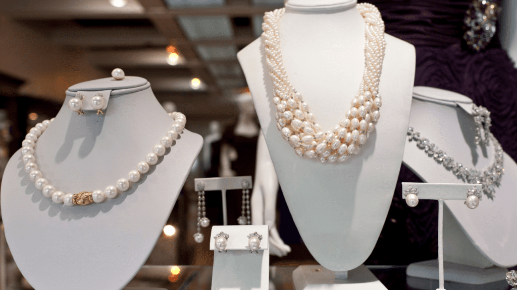 Elegant pearl jewelry display with single and multi-strand necklaces, matching earrings, and bracelets on white stands, shining under soft lighting.
