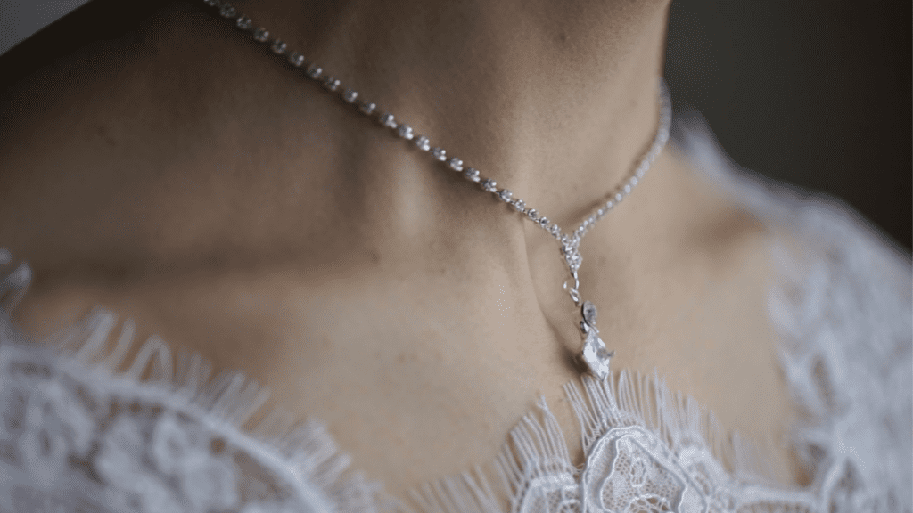 
A delicate silver necklace with a sparkling pendant adorns a woman's neck, complementing her lace-trimmed outfit and adding an elegant touch.
