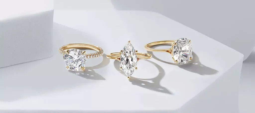 
ChatGPT
Three gold engagement rings, each with a distinct diamond cut—round, marquise, and oval—are elegantly displayed on a white geometric surface.