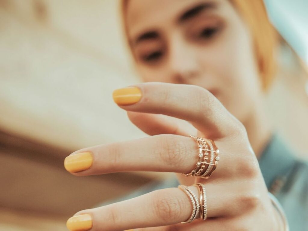 Stylish woman with yellow nail polish displaying multiple intricately designed rings on her fingers, creating a modern and chic look