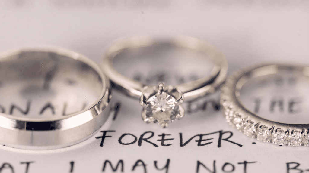 Three rings, including a solitaire diamond engagement ring, placed on a handwritten note with the word "forever," symbolizing eternal love and commitment.