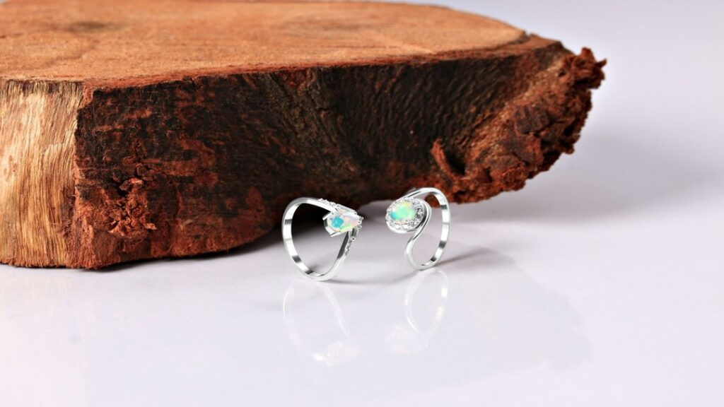 Delicate silver rings adorned with opal stones displayed against a rustic wooden block backdrop, highlighting their vibrant iridescence and elegance.