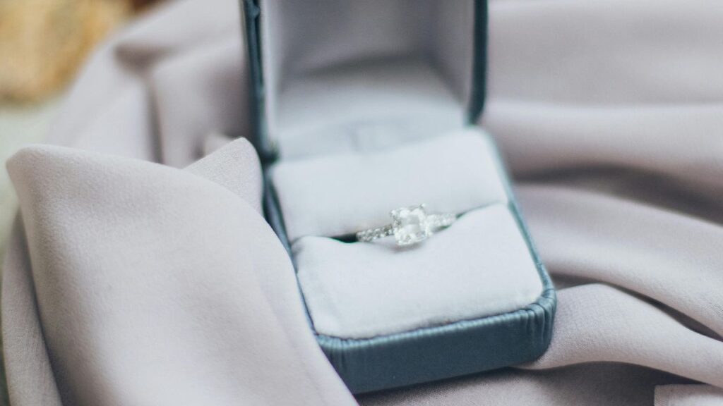 Elegant diamond ring displayed in a velvet-lined box, surrounded by soft, draped fabric, highlighting the ring's brilliance and luxurious presentation.