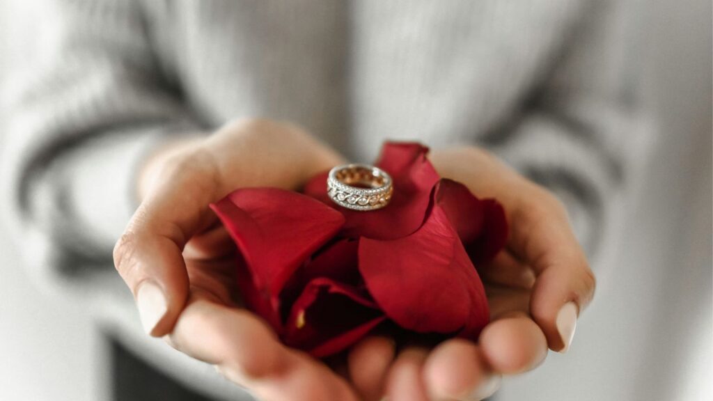 Intricately designed ring placed on red rose petals, held gently in hands, symbolizing love, care, and the beauty of fine craftsmanship.