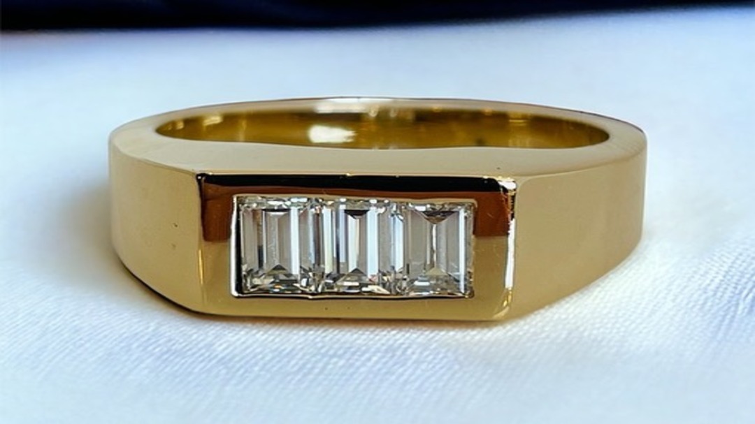 Close-up of a sleek gold ring featuring a rectangular setting with five vertical baguette-cut diamonds, resting on a white fabric surface.