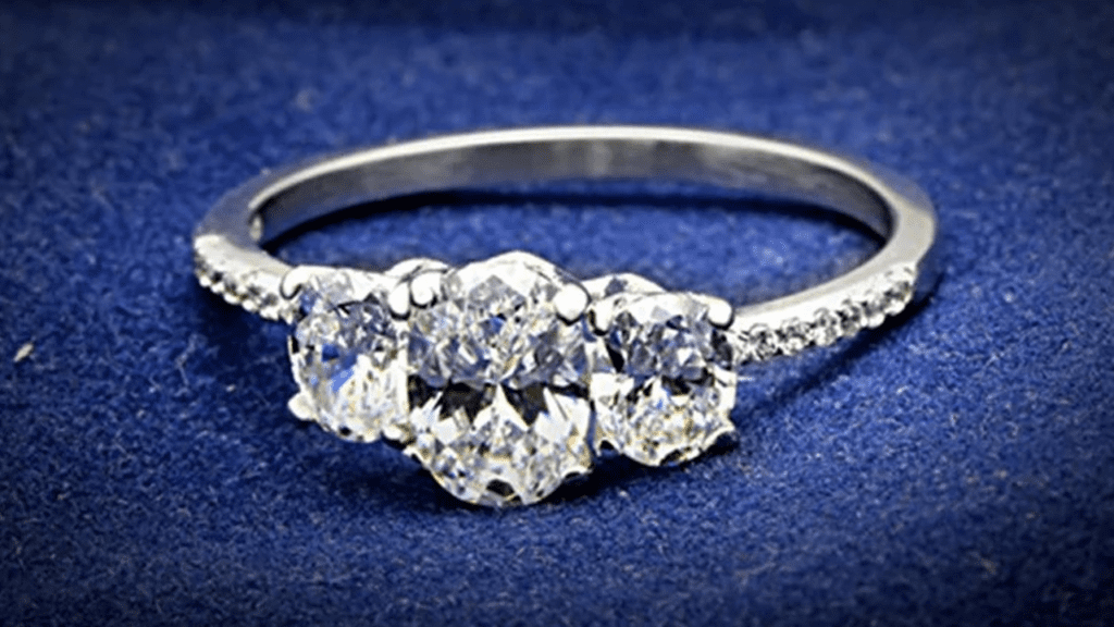 A stunning three-stone diamond ring with a sparkling trio of round-cut diamonds on a delicate band, set against a deep blue fabric backdrop.