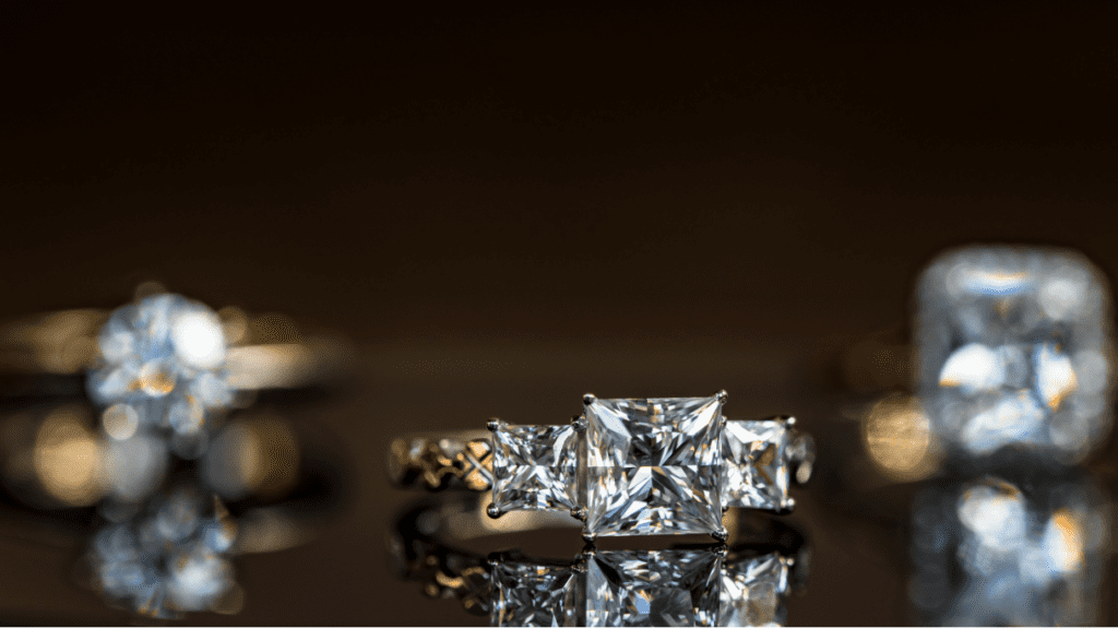 Three rings with dazzling square-cut diamonds. The central ring features a trio of square diamonds, while the others are softly blurred in the background.