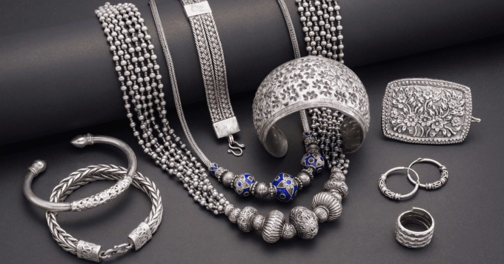 A collection of intricate silver jewelry including bracelets, necklaces, rings, and a buckle, beautifully arranged on a dark background.