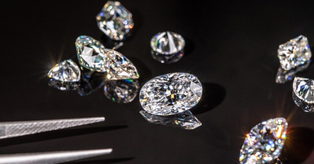 Scattered cut diamonds sparkle brilliantly against a dark background, with a pair of precision tweezers poised to pick one up, showcasing their clarity.