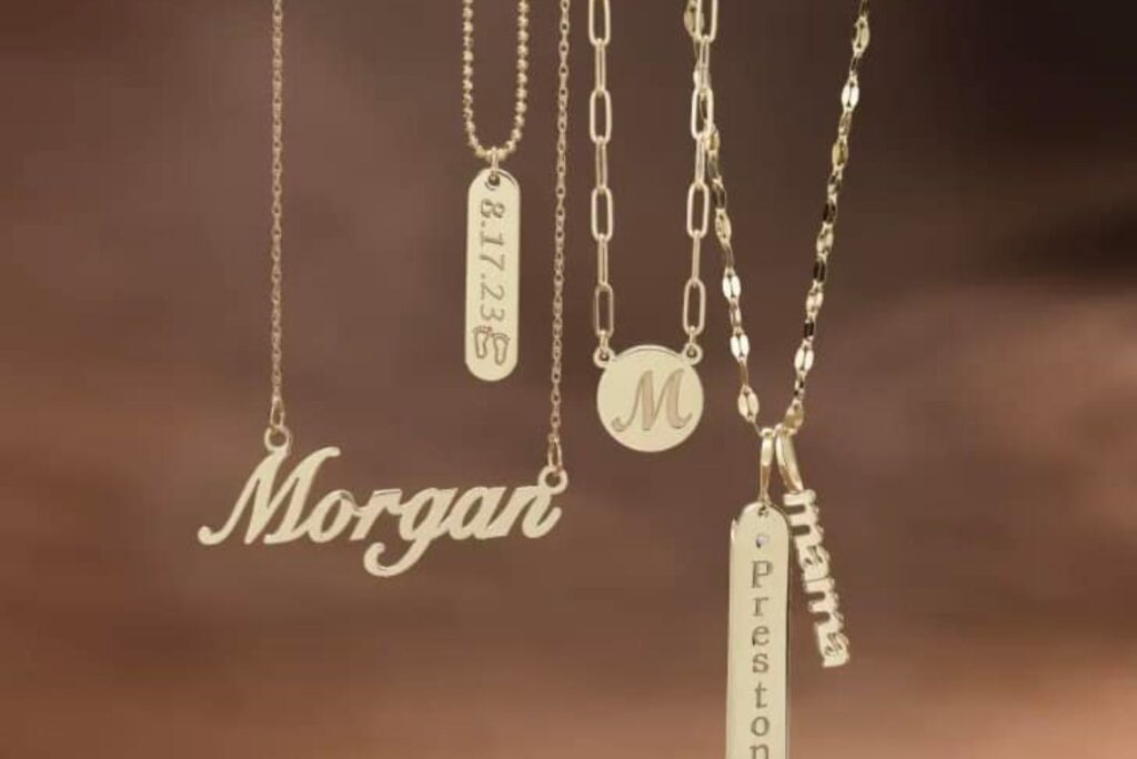 A collection of gold necklaces with personalized name and initial pendants, featuring names like Morgan, Preston, and dates on rectangular tags.