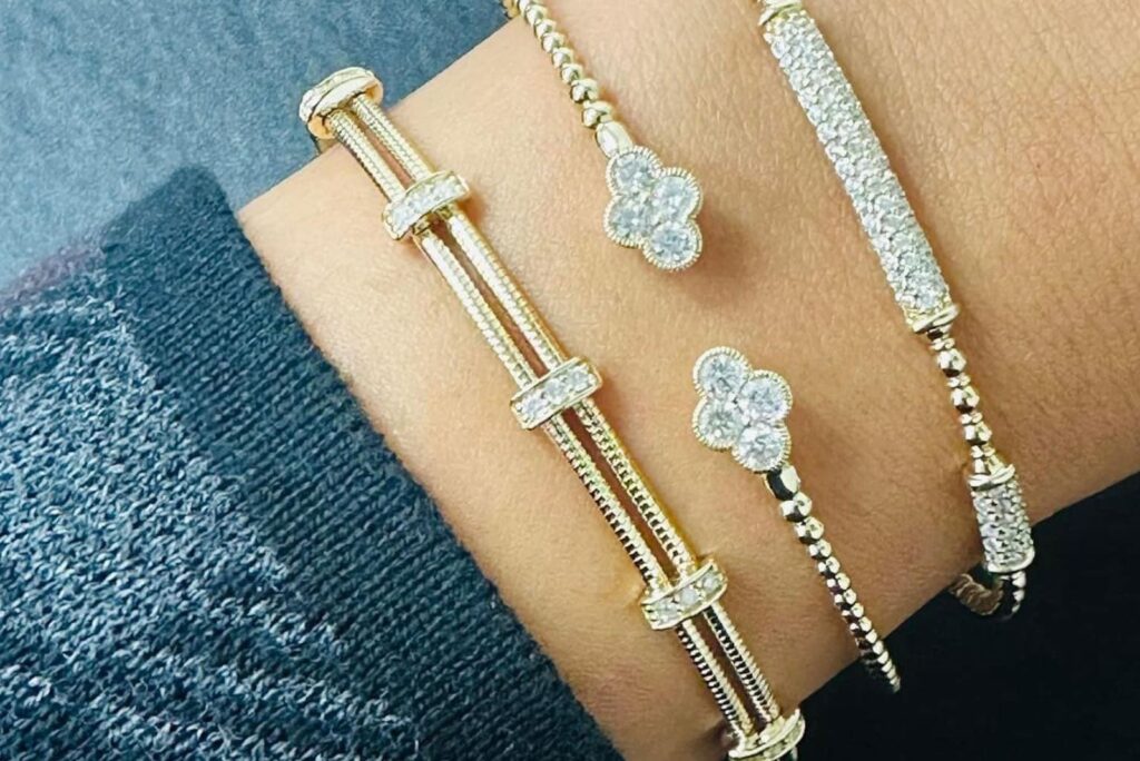Three gold and diamond bracelets with intricate designs are showcased on a wrist, highlighting elegant craftsmanship and luxurious appeal.