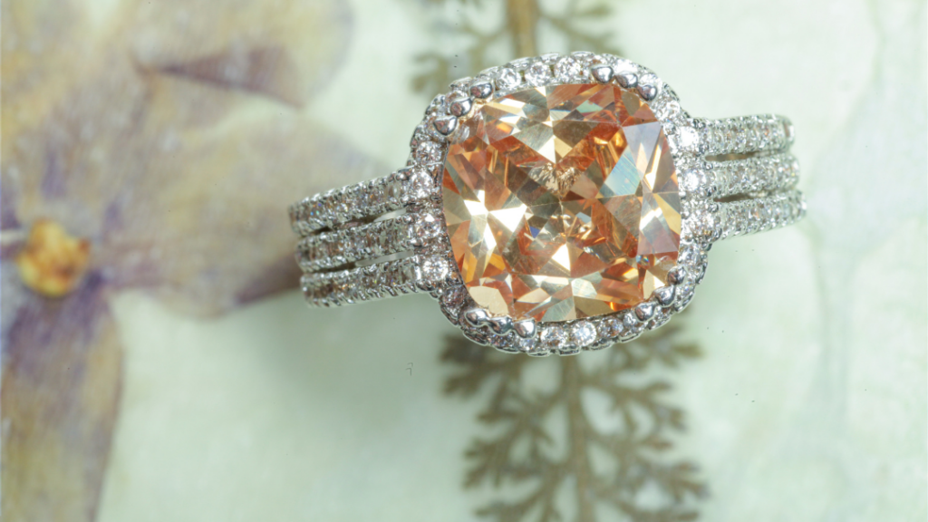 Elegant ring featuring a large cushion-cut orange gemstone surrounded by a halo of small diamonds, set on a triple diamond-encrusted band.