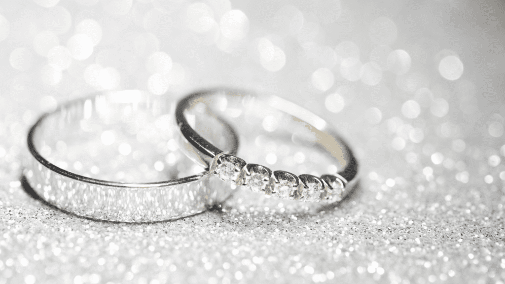 Close-up of two wedding bands, one plain and one adorned with diamonds, placed on a shimmering silver surface, highlighting their brilliance.