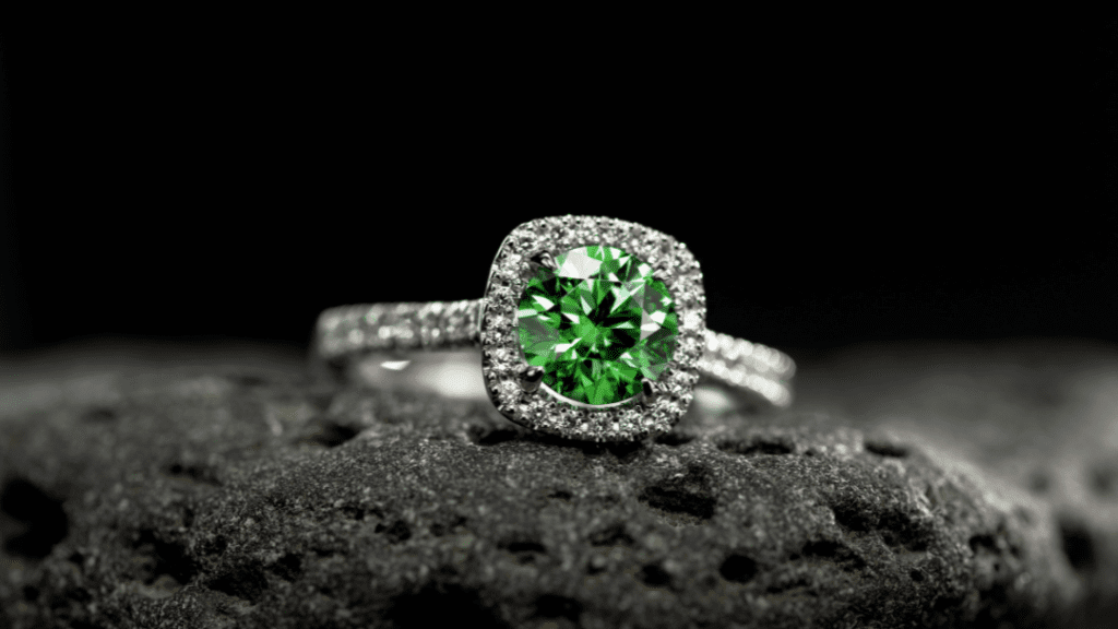 A stunning silver ring featuring a vibrant green gemstone at its center, encircled by a halo of sparkling diamonds, set against a textured rock.