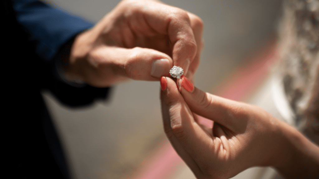 Close-up of a man holding a woman's hand as he places a sparkling diamond engagement ring on her finger, capturing a romantic moment.