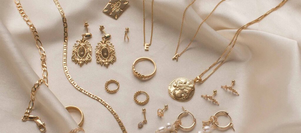 A collection of elegant gold jewelry, including necklaces, rings, earrings, and bracelets, arranged artistically on a smooth, light-colored fabric.