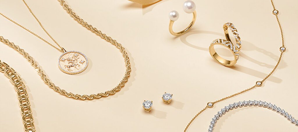 A collection of gold jewelry featuring various designs: a pearl ring, a braided chain necklace, a coin pendant, a diamond bracelet, and stud earrings.