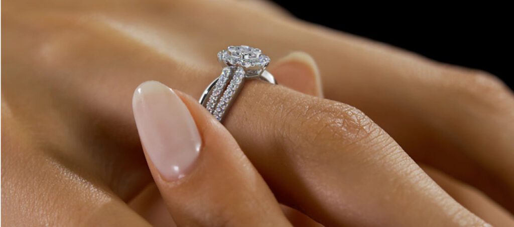 A woman's hand with a polished manicure elegantly showcases a diamond-encrusted engagement ring against a soft-focus black background.