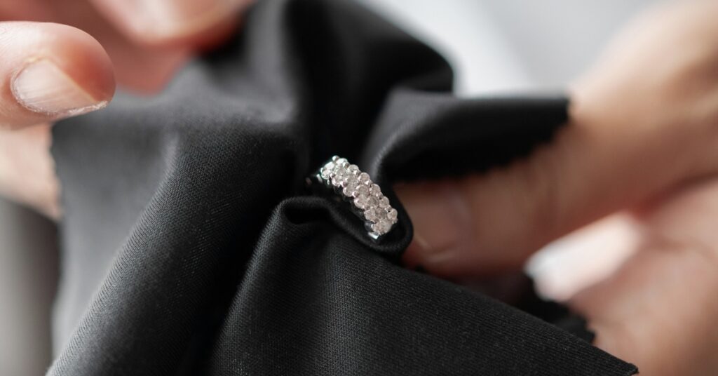 Close-up of a person using a black cloth to polish a diamond ring, highlighting the meticulous care and attention to maintaining its sparkle.