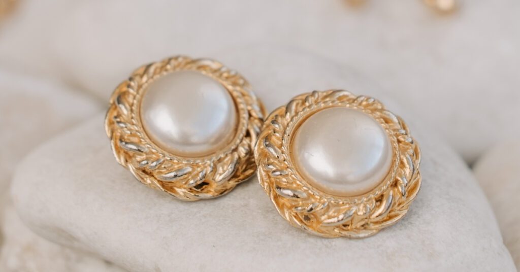 Elegant pearl earrings set in intricate gold frames, placed on a soft, light-colored surface, showcasing their timeless and luxurious design.