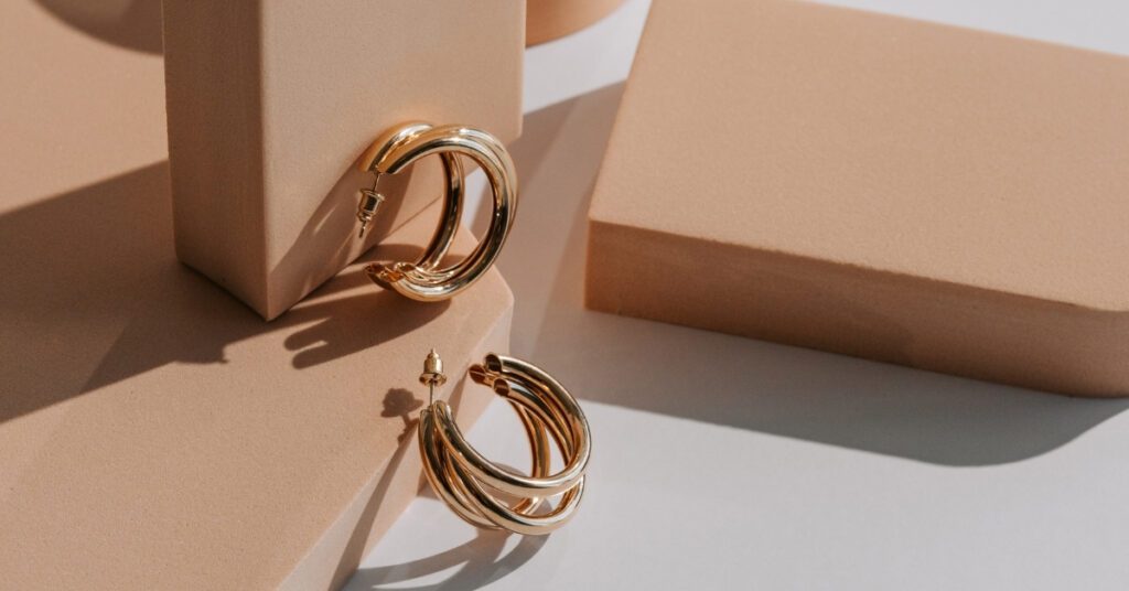 Elegant gold hoop earrings displayed on geometric beige blocks, casting shadows in soft natural light, highlighting their shiny and stylish design.