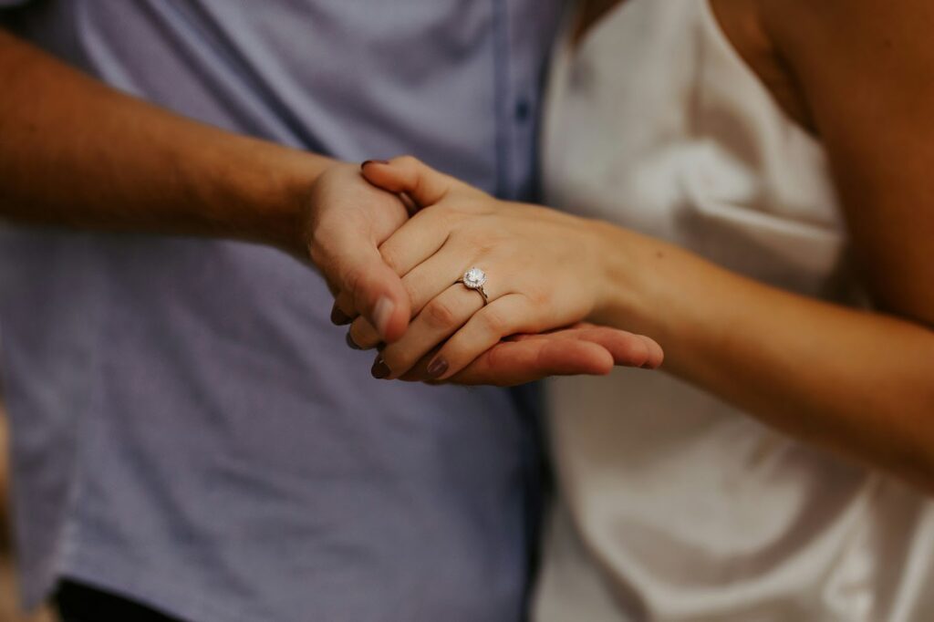 A close-up of two people holding hands, showcasing an elegant engagement ring on the woman's finger, symbolizing love and commitment.