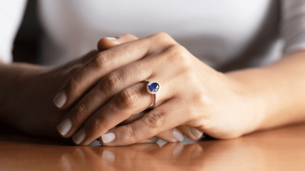 Close-up of hands with a sapphire engagement ring, showcasing a deep blue gemstone set in a delicate band, symbolizing elegance and timeless beauty.