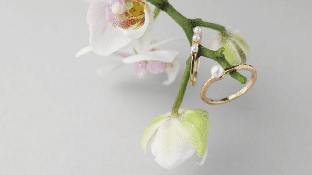 Elegant gold rings with pearls hang delicately from a blooming orchid, showcasing nature's beauty intertwined with exquisite jewelry design.