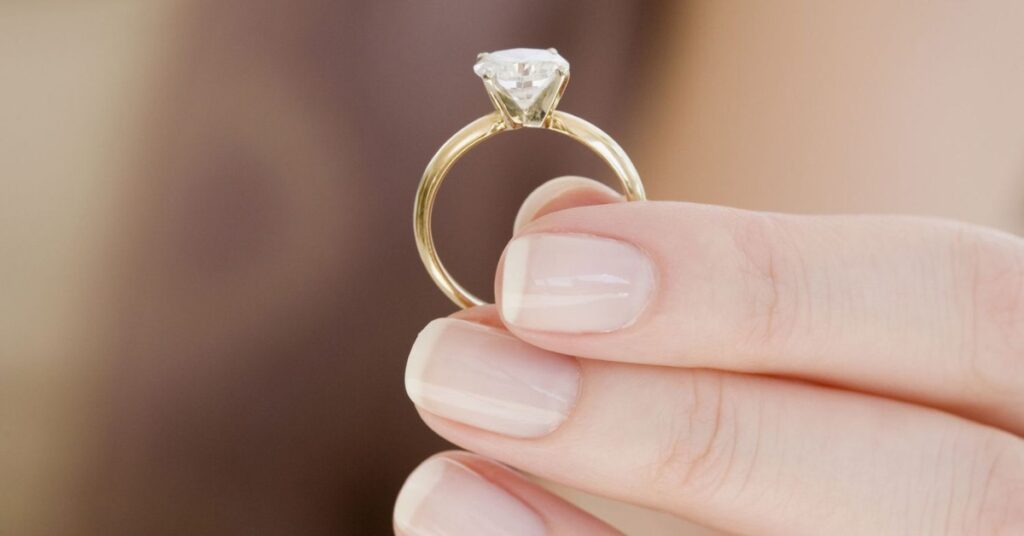 A well-manicured hand holds a gold ring with a brilliant-cut diamond, emphasizing the clarity and craftsmanship of the fine jewelry piece.