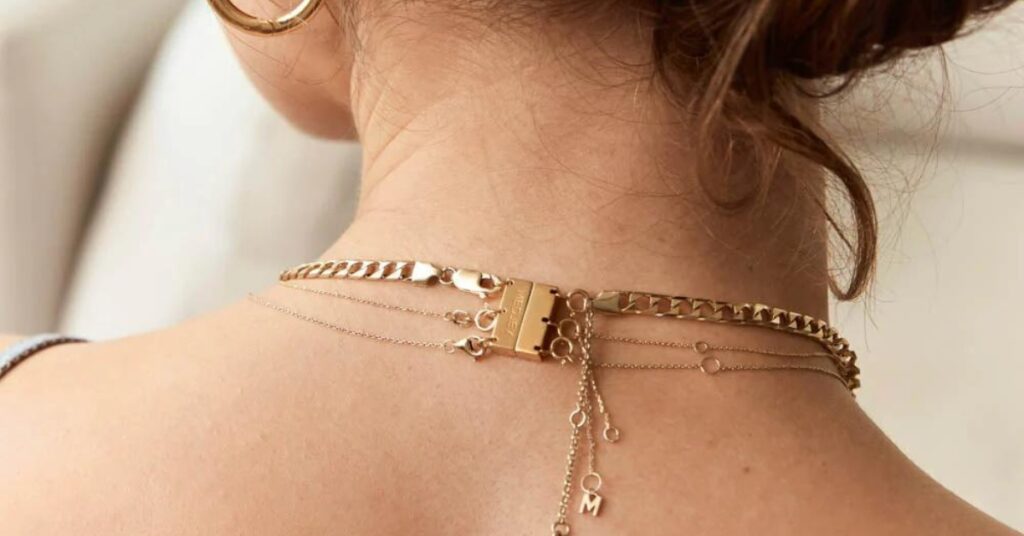 A close-up view of the back of a woman's neck adorned with layered gold necklaces, featuring delicate chains and a bold clasp.