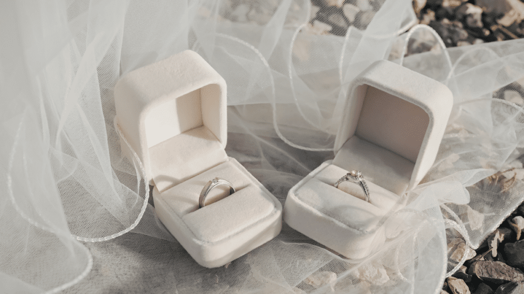 Two velvet ring boxes holding elegant diamond rings, placed on a soft white fabric, symbolizing the delicate beauty of a wedding or engagement.