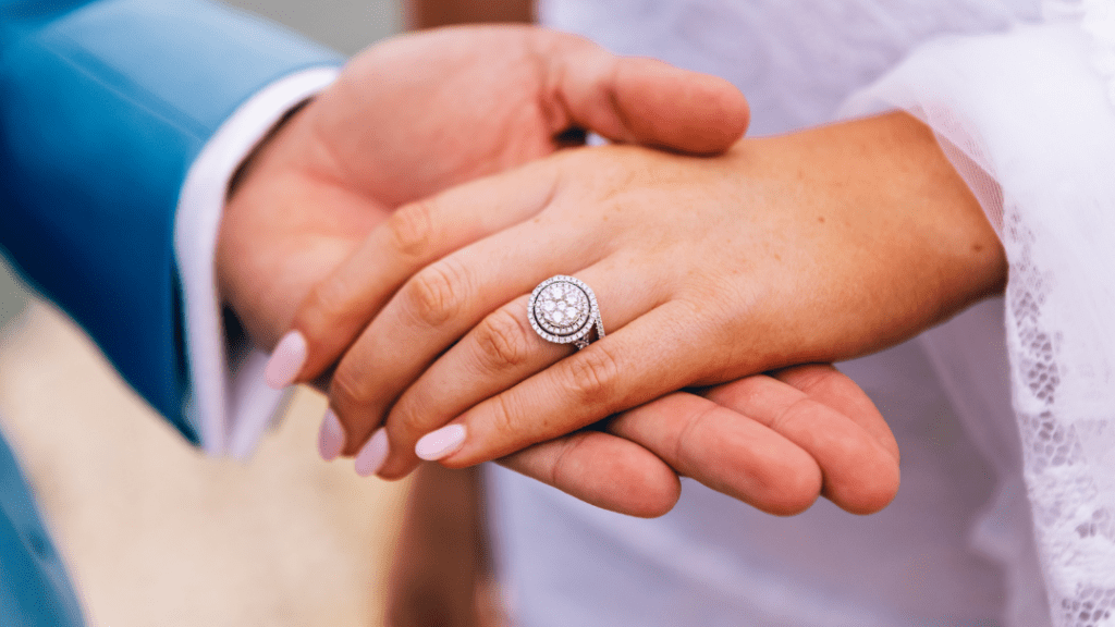 Close-up of intertwined hands, one with a glittering diamond-studded ring, signifying love and commitment, against a soft, blurred background.