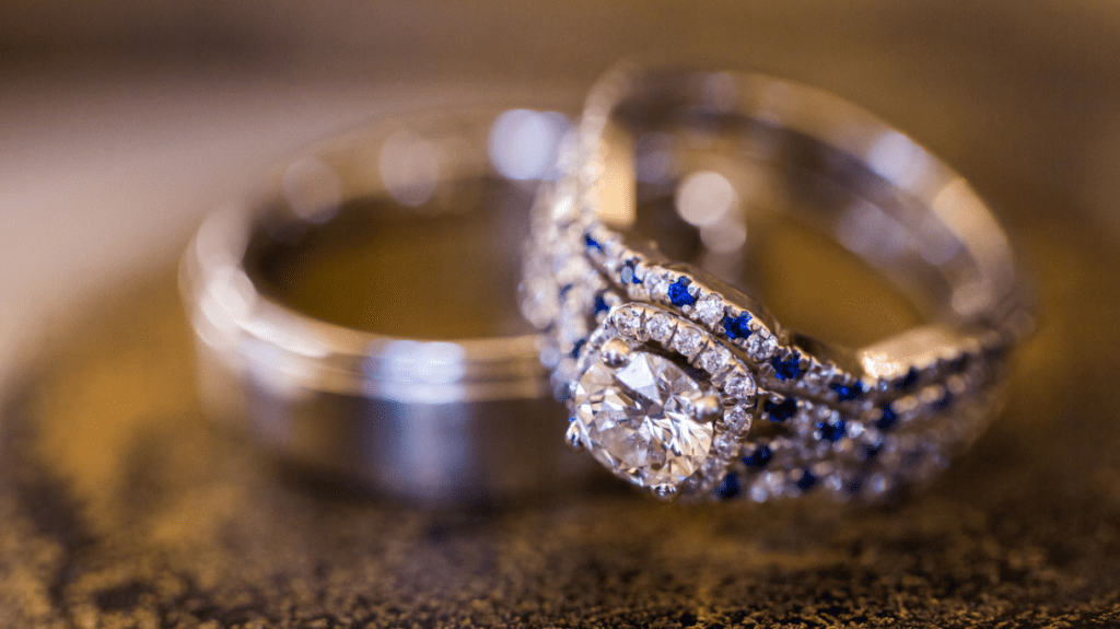 A close-up of an elegant diamond ring adorned with small blue stones, paired with a polished wedding band, capturing the essence of timeless romance.