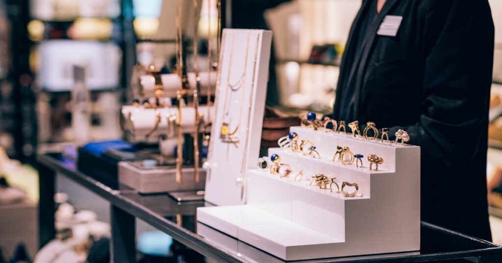 A display of gold rings with blue gemstones on a tiered white stand in a jewelry store. 

