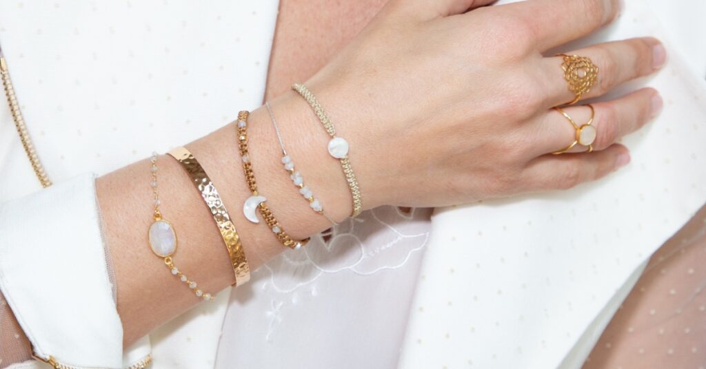 A close-up of a woman's hand wearing a variety of gold jewelry, including bracelets and rings with white gemstones. 

