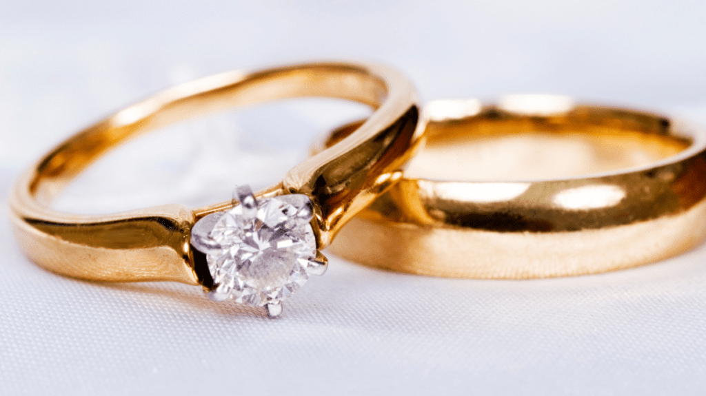 Two gold wedding rings, one with a solitaire diamond, shine on a white background, symbolizing elegance, commitment, and timeless love.