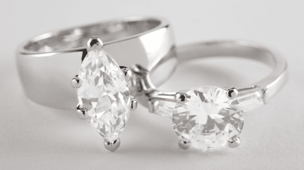 A close-up image of a pair of elegant diamond rings; one features a marquise-cut stone, while the other showcases a round brilliant-cut diamond.