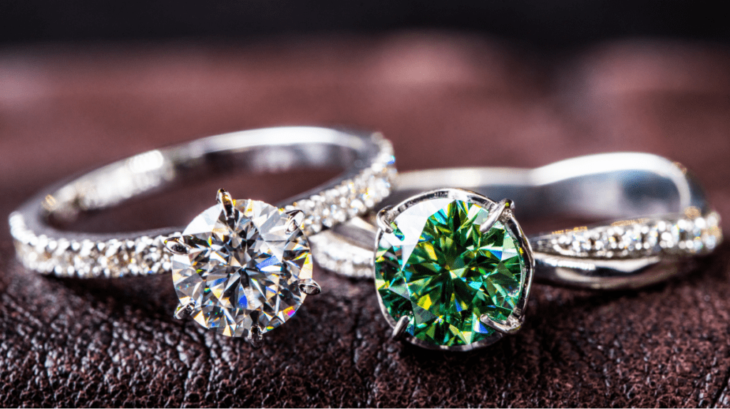 Two exquisite engagement rings side by side: one features a dazzling round-cut diamond, the other showcases a vibrant green gemstone.