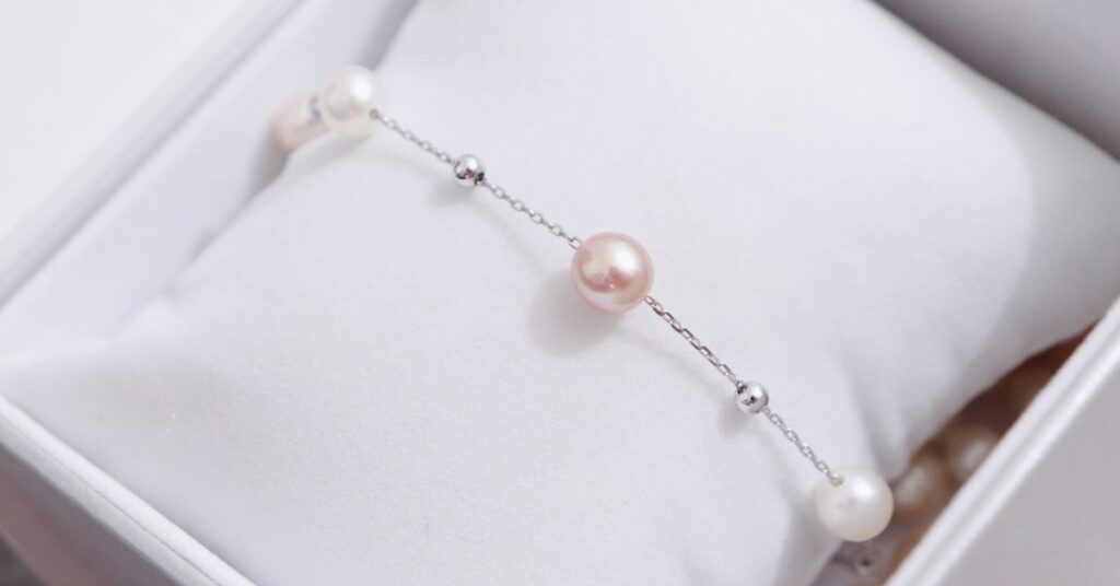 A delicate bracelet with pink and white pearls and silver beads, elegantly displayed on a white cushion inside a jewelry box.