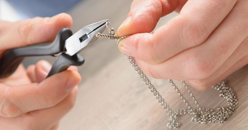 Hands meticulously repairing a silver chain necklace using pliers, showcasing precision and attention to detail in jewelry craftsmanship.