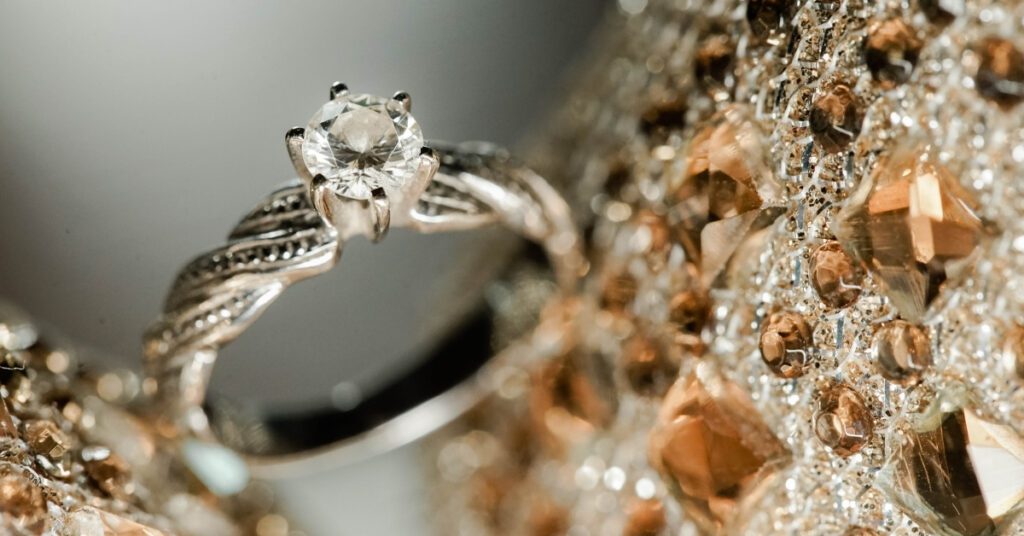 A close-up of a solitaire diamond ring with intricate detailing, set against a background of sparkling, gold-hued gemstones, highlighting its elegance.