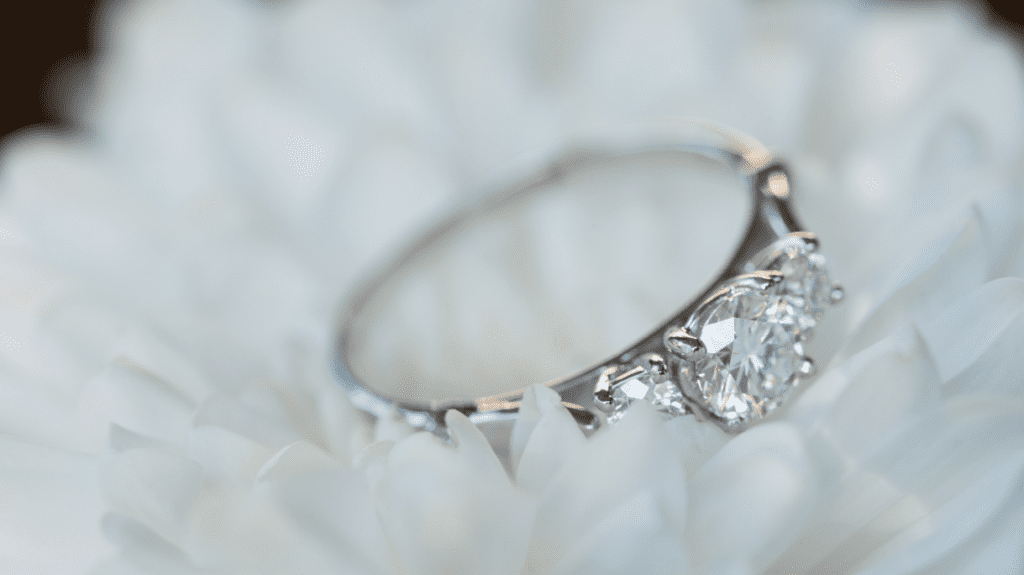 A dazzling diamond engagement ring with a trio of round-cut diamonds set in a silver band, displayed on a soft white chrysanthemum.