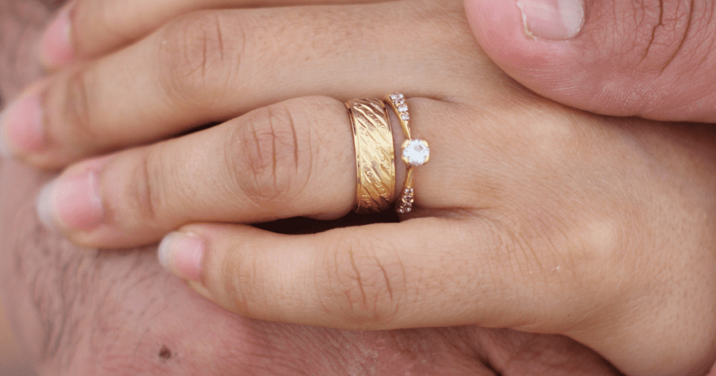 Close-up of intertwined hands, showcasing gold wedding bands with intricate designs and a diamond ring, symbolizing love and commitment.