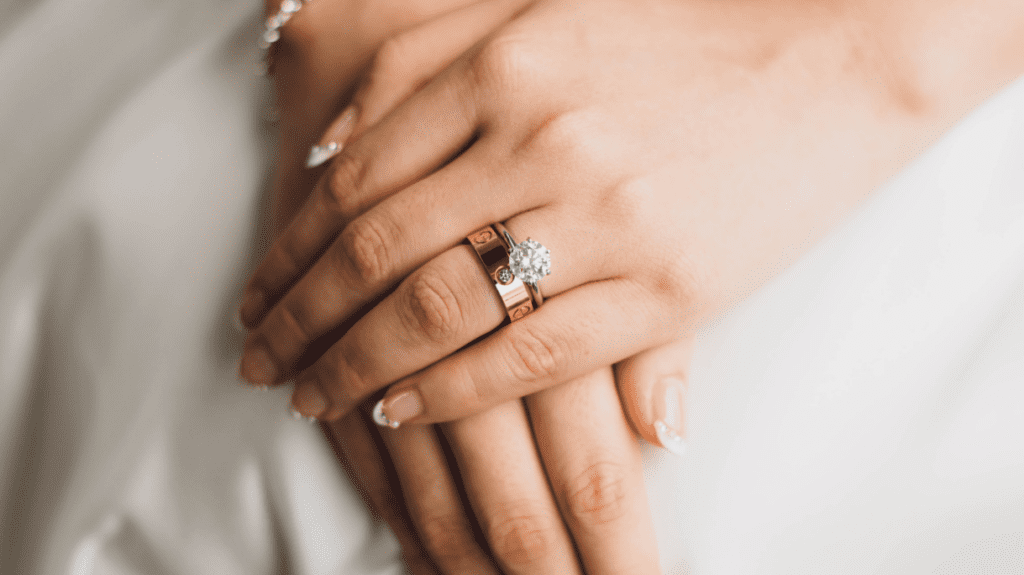 Close-up of hands showcasing a sparkling diamond engagement ring paired with a golden band, highlighting elegant and manicured nails.