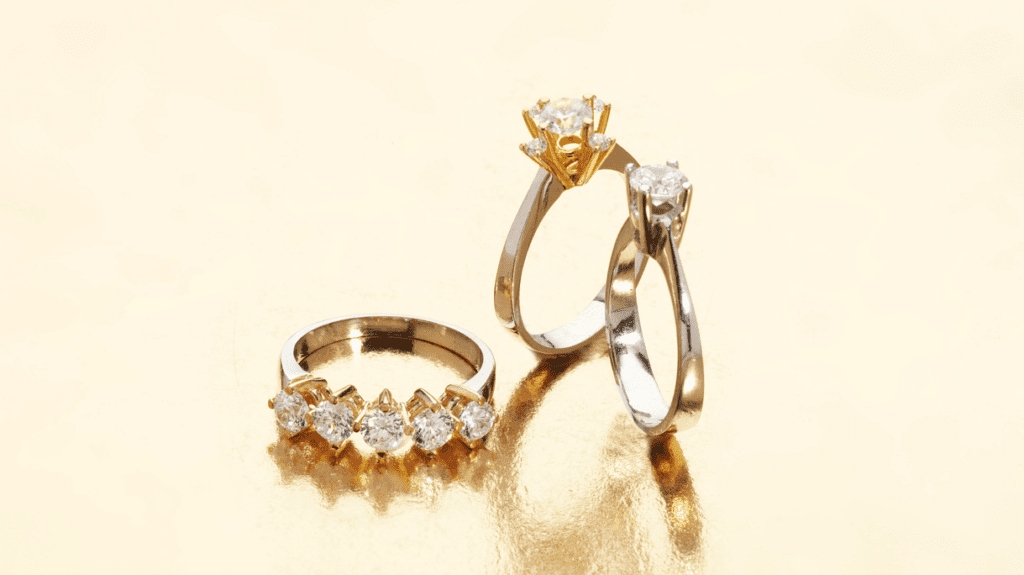 Three elegant diamond rings in gold and silver settings, showcased against a shimmering golden backdrop.