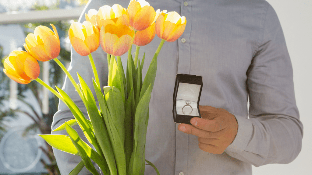 Man holds tulips and a ring box, ready for a romantic proposal.