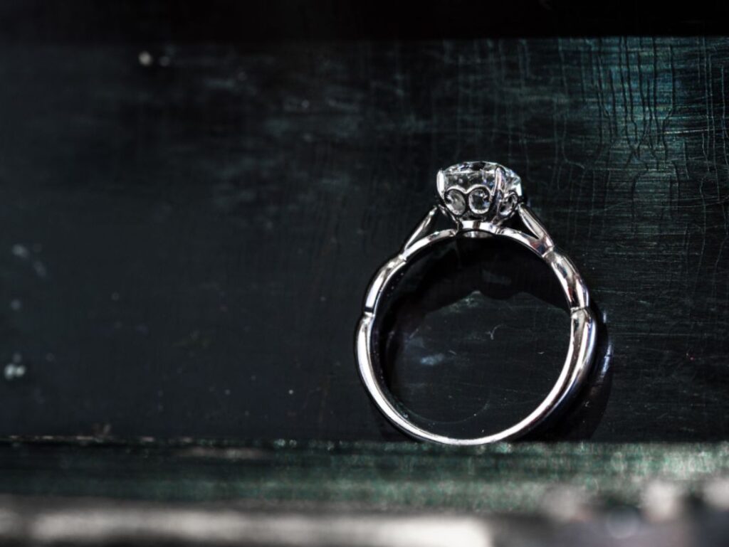 A solitaire diamond ring with intricate prongs, showcased on a dark, textured surface, emphasizing the ring's elegant and refined design.