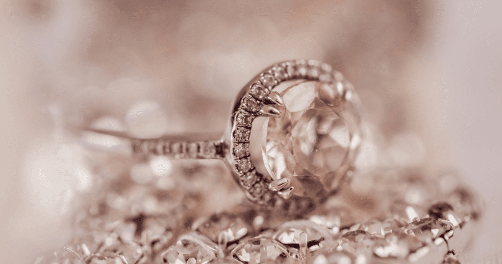 A delicate ring featuring a large, light pink gemstone surrounded by a halo of smaller diamonds, displayed on a shimmering, blurred background.