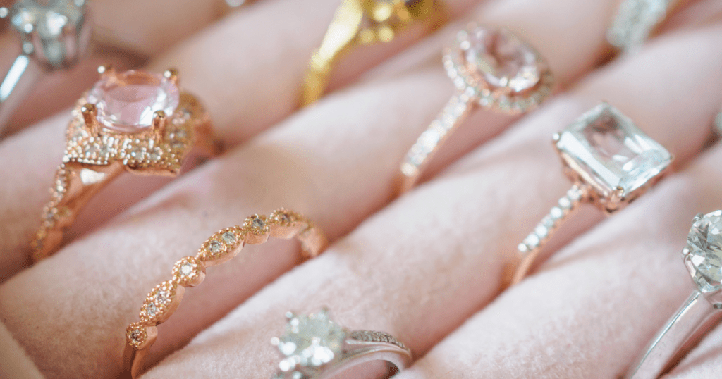 A collection of elegant rings displayed on a pink velvet holder, featuring intricate designs and gemstones in rose gold and silver settings.